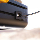 A close-up of a black cable secured by a small black bracket attached to a metal surface, with a blurred outdoor background—ideal for use with tent accessories or spring rod holders such as the CVT Mt. Hood Spring Rod Holder - 2 Pack.