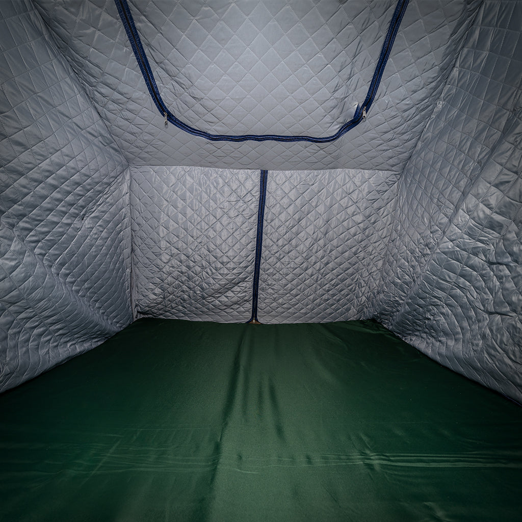 Interior view of an empty CVT tent featuring Pioneer Insulation Walls with quilted silver fabric and diamond-patterned stitching, a green floor, and zippered openings—designed for cold weather camping.