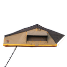The CVT Pioneer 2 Softshell Tent, featuring a tan body, black rainfly, and yellow trim, is mounted on a vehicle roof rack—ideal for overland adventures. A collapsible ladder provides access to the tent, while the open front window reveals its inviting interior.