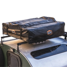 A black CVT rooftop tent is securely mounted on top of a green vehicle with a roof rack. The tent is folded and protected by the Pioneer Travel Cover from CVT, which features weather-resistant material and displays the CVT logo with orange and white accents.