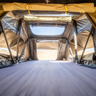 Gazing out from inside a roomy rooftop tent through open mesh windows to a sunlit landscape, the spacious sleeping area features the CVT Pioneer Mattress Cover and neatly rolled-up canvas flaps.