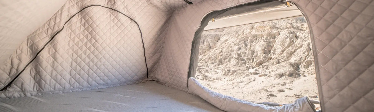 Interior of a light gray quilted tent with a large open window, showing a rocky, sandy outdoor landscape and letting in natural light. The tent appears clean and spacious.