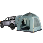 A gray SUV is parked with a large Timber Creek SUV Tent by CVT, in green, attached to its rear, creating a sheltered space that connects the vehicle to the tent. With mesh windows and a dome-style design, this tent is set up for camping—making it an ideal choice for overlanders seeking comfort and convenience on their adventures.