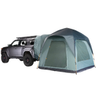 A gray SUV with a roof rack is parked next to a large CVT Timber Creek SUV Tent, which features a dome-style design and attaches directly to the back of the vehicle, creating an integrated camping setup perfect for overlanding.
